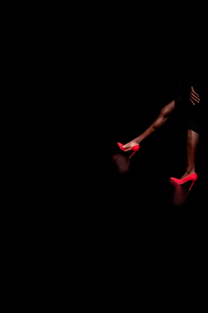 Reflet d’Audace : une silhouette élégante, un éclat rouge vibrant dans l&#039;obscurité, capturant le mystère et la sensualité sur une scène théâtrale.