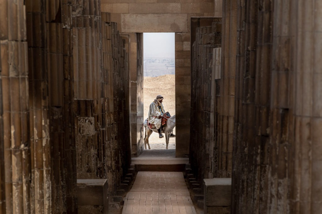 Taxi illustre un instant unique à Saqqarah, où un homme sur une mule traverse le seuil entre l&#039;ancien et le moderne, incarnant l&#039;essence du voyage dans une toile traditionnelle et contemporaine, enracinée dans la série &quot;Mikado&quot;.