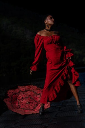 Dans Rose Obsidienne, la lumière sculpte la force. Rouge, noire et souveraine, cette femme semble naître du feu et du silence.