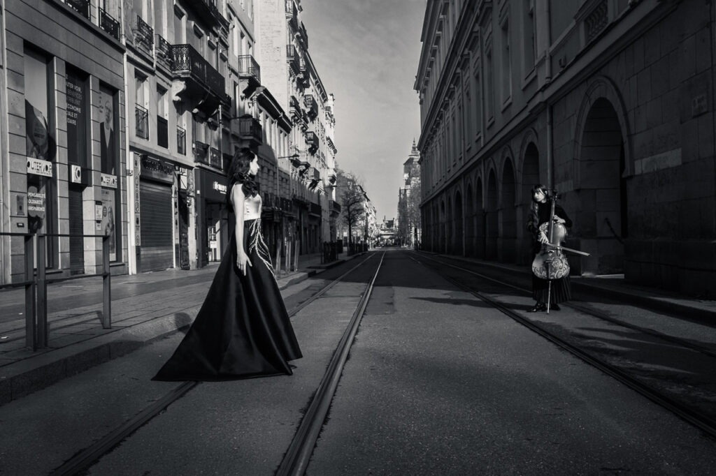 L'Ecart Photo noir et blanc artistique de deux femmes dans une rue vide avec perspective centrale, ambiance cinématographique et tension visuelle.