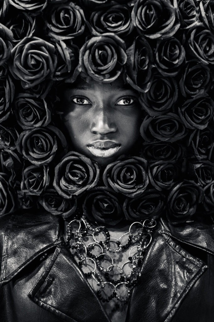 Le Poids des Fleurs Portrait femme noir et blanc artistique avec fleurs sombres, regard intense, photographie d’art en tirage limité pour décoration murale.