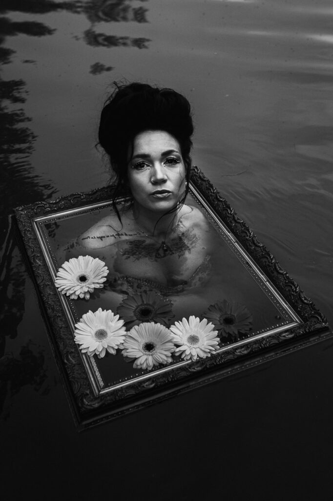 Encadr&eacute;e Vive, photographie de Thierry Stentzel : portrait noir et blanc d&rsquo;une femme immerg&eacute;e, visage &eacute;mergeant d&rsquo;un cadre ancien parmi des fleurs.