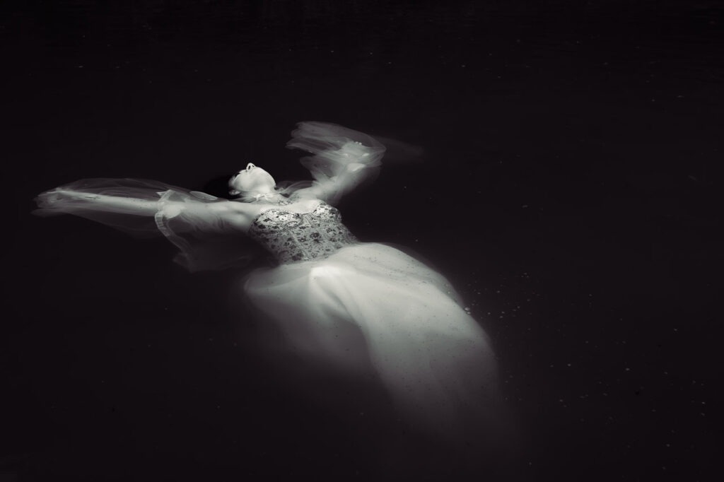 Sainte Dérive Sainte Dérive de Thierry Stentzel, photographie d’art noir et blanc d’une femme en robe blanche flottant sous l’eau.